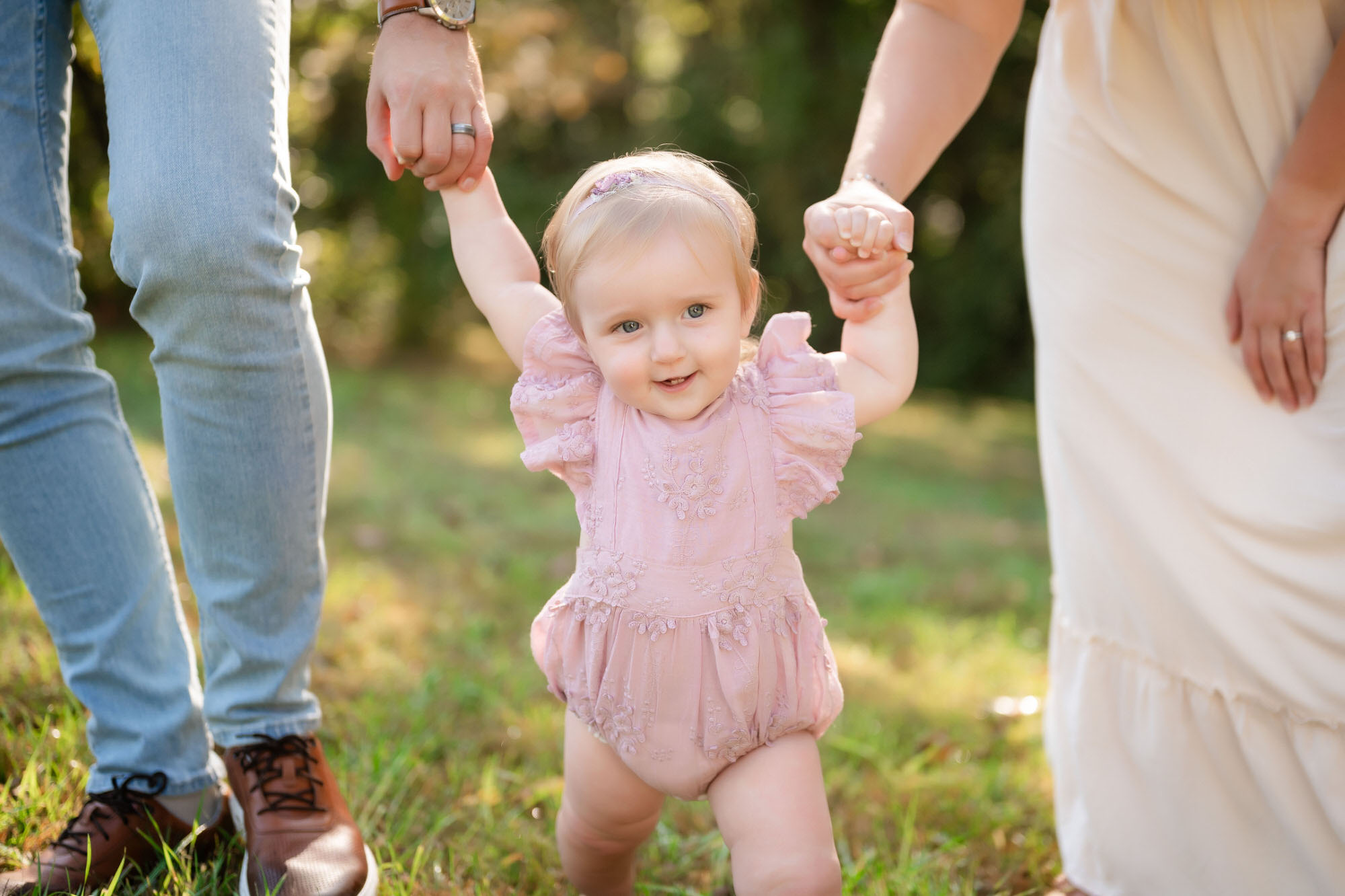 cute baby girl smiling and holding parents hands during outdoor pittsburgh family photography session • Family